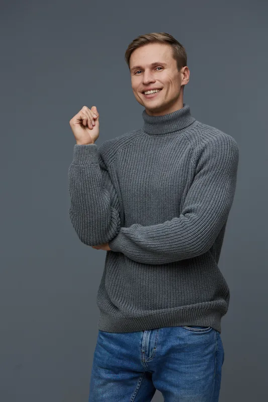 smiling young caucasian man wear gray knitted turtleneck pullover blue jeans standing isolated on gray background mental health and gadgets concept