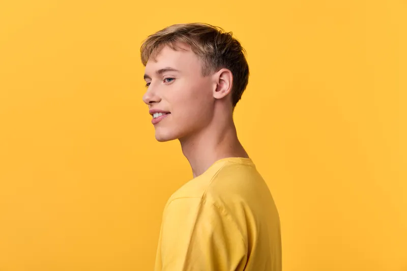 Young man in side profile against a yellow background wearing a yellow shirt, minimalist studio shot with soft lighting, capturing a calm, confident mood for fashion and lifestyle use