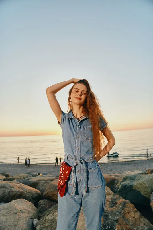 lifestyle woman in modern boho-western denim street style enjoys sunset at the beach with relaxed pose and film color tones creating a warm atmosphere