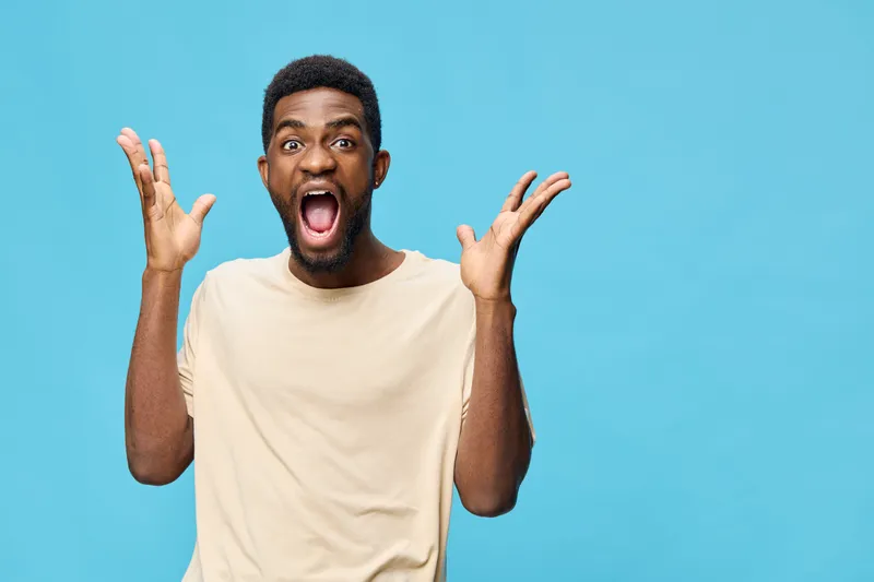 Young man expressing surprise and excitement with open hands and a joyful facial expression against a vibrant blue background, perfect for conveying emotions