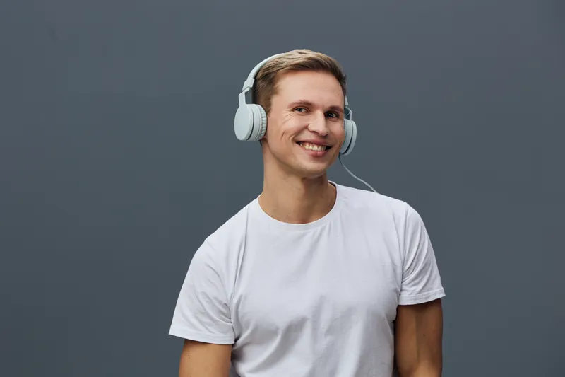 Smiling young man wearing headphones, casual white t-shirt, looking at camera, isolated on plain gray background, studio portrait, lifestyle concept