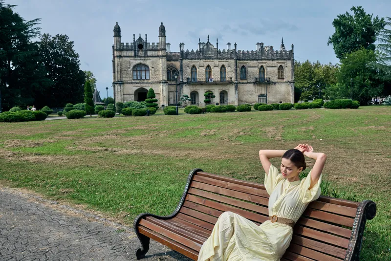 Woman on a bench in a park with a castle in the background, outdoor leisure and travel scenery highlighting architecture and historic relaxation.