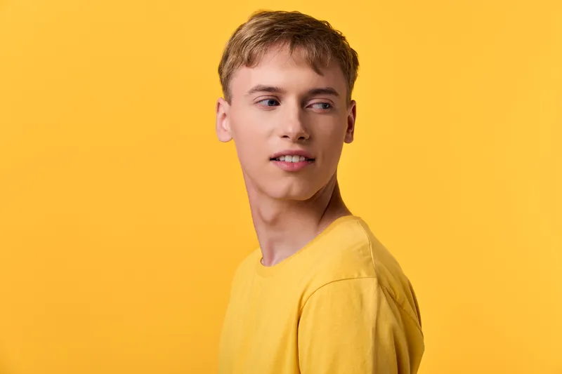 Young man in yellow shirt against a bright yellow background with casual pose and subtle smile, modern style for fashion and lifestyle themed advertising and branding projects