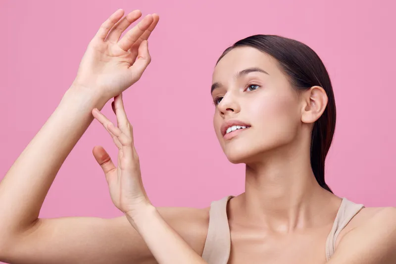 Young woman with natural beauty demonstrating a fresh skincare routine against a soft pink background, showcasing confidence and tranquility in a modern style