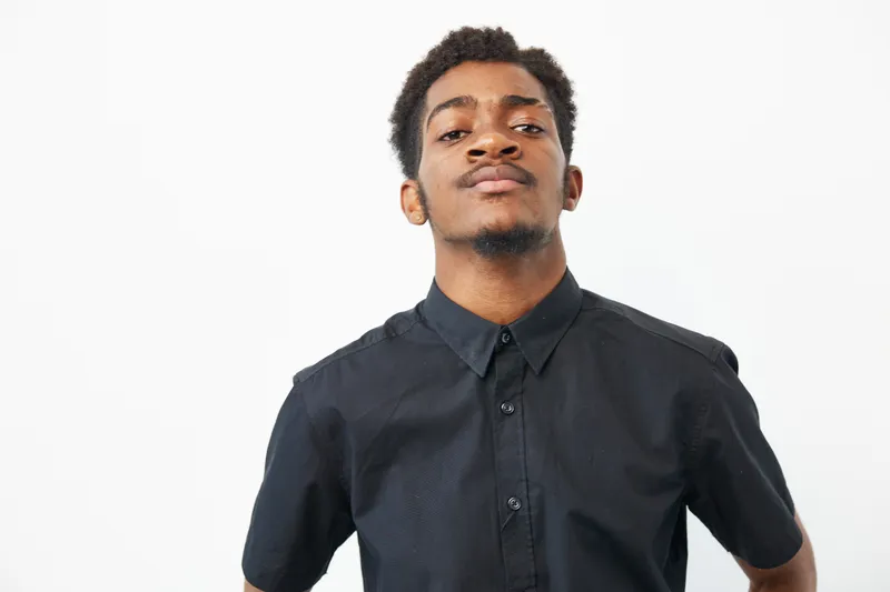 Confident black man in a casual black shirt, showcasing self-assurance and style. The image captures a strong presence against a clean background.