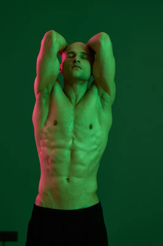 Athletic man posing confidently against a green backdrop, showcasing strength and fitness in a creative, energetic atmosphere. A vibrant approach to modern male portraiture.
