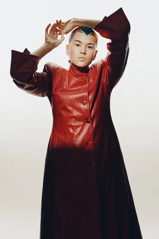 young woman posing confidently in a long red leather coat with stylish short hair, clean white background, modern fashion and individuality expression, studio lighting
