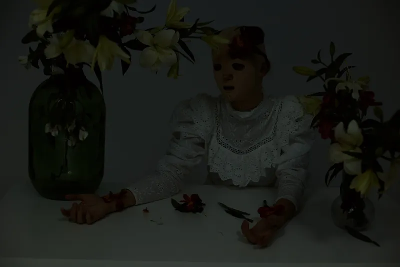 A melancholic female model in a vintage lace dress surrounded by dark floral arrangements, expressing sadness and introspection in a moody and artistic setting