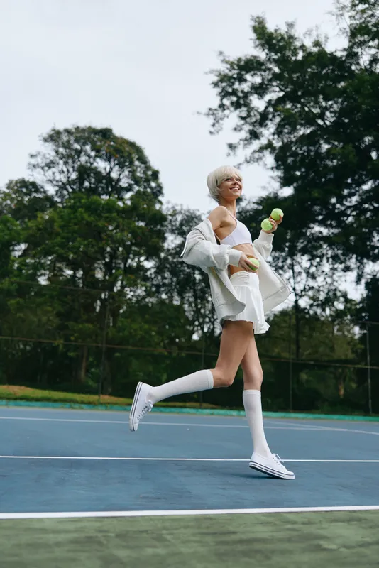 Joyful female tennis player in sporty outfit running on court with tennis balls, showcasing energy and enthusiasm, perfect for sports and fitness themes