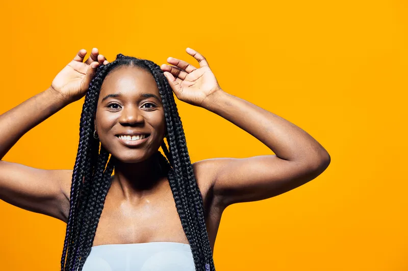 Smiling African woman with braided hair against a vibrant yellow background, showcasing joy and confidence in a modern hairstyle