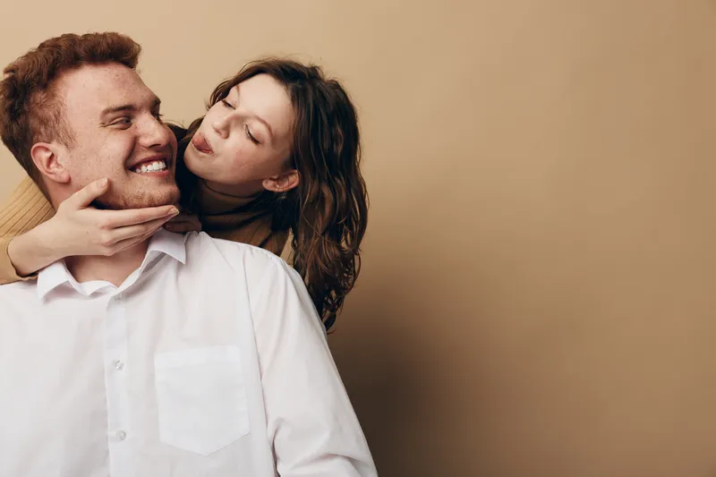 Happy young couple embraces and smiles in casual clothes against beige background. Concept of love, relationship, affection, and joyful moments between man and woman.