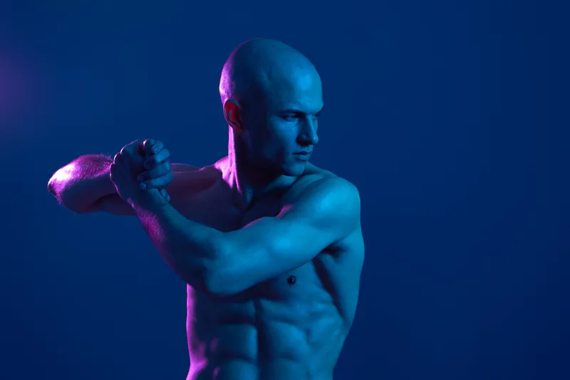 Strong man posing in dramatic blue lighting, showcasing athletic physique and determination, perfect for fitness and motivation themes.