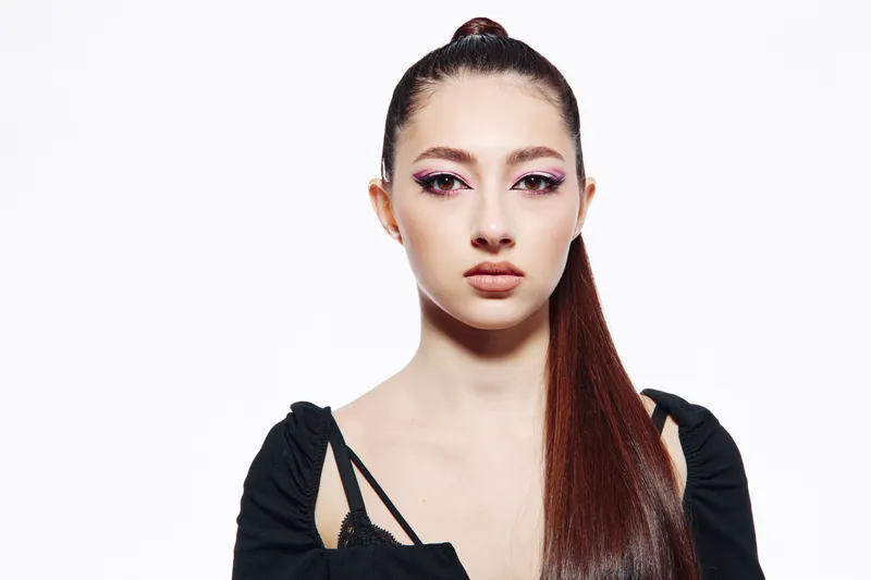 Young woman with bold dramatic makeup and sleek long hair posing with serious expression on white background. Concept of beauty fashion creative portrait and makeup style.