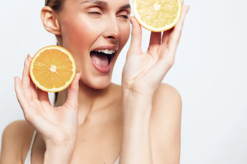 Happy woman holding orange and lemon slices near her face smiling with closed eyes. Bright white background. Concept of healthy lifestyle, freshness, and natural beauty.