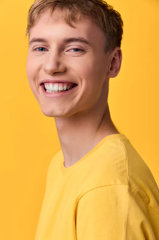Smiling man in a yellow shirt against a vibrant yellow background, warm studio lighting highlights friendly expression and casual style, suitable for lifestyle or fashion branding and advertisements