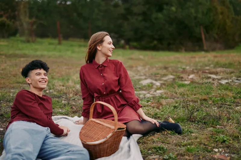 A candid outdoor scene shows two friends relaxing on a blanket with a wicker basket, a genuine smile highlighting authenticity and credibility in a natural setting.