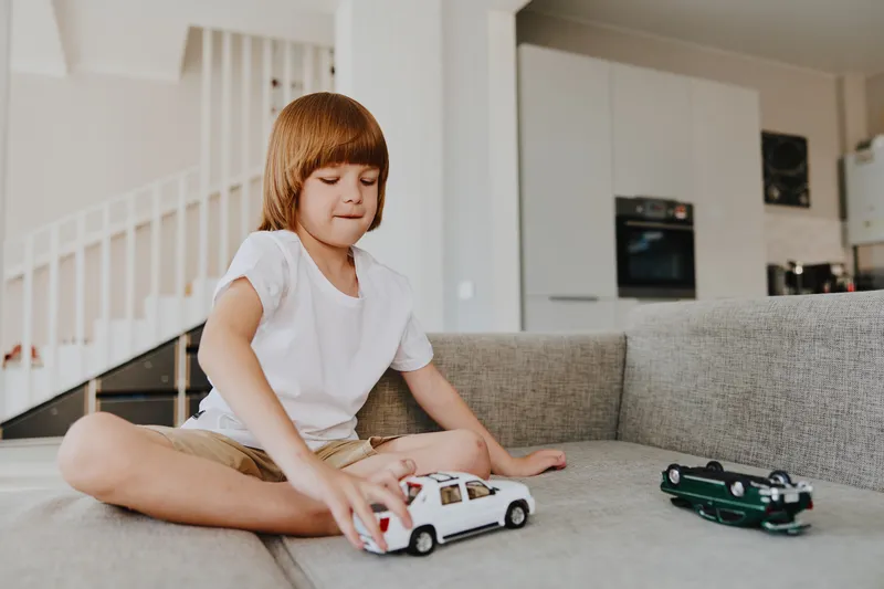A focused boy playing with toy cars, showcasing creativity and playfulness in a modern living room setting, surrounded by soft colors and natural light.