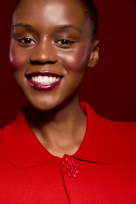 Close-up portrait of smiling African woman with dark skin wearing red blouse against red background. Concept of beauty, fashion, confidence, and elegance with vibrant colors and studio lighting.