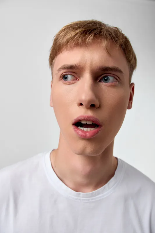 Surprised man face expression close up in a white t shirt, wide eyes and open mouth convey astonishment, curiosity and a spontaneous reaction in a minimalist studio setting