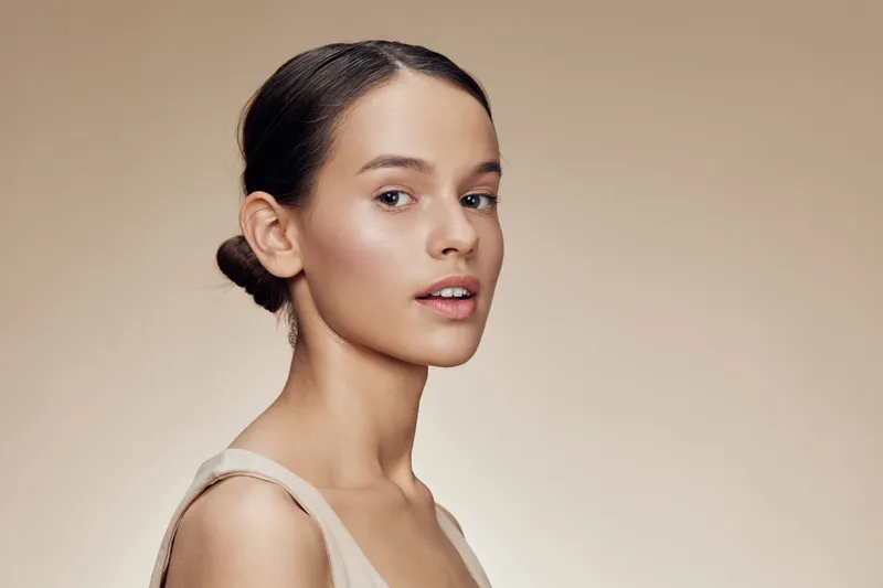 Elegant young woman with a serene expression in a neutral toned background, perfect for beauty and skincare concepts, showcasing natural beauty and simplicity