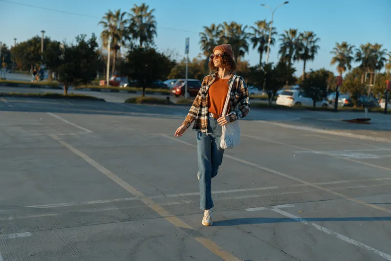 woman walking in a parking lot, casual urban portrait at golden hour glow, candid lifestyle shot with authenticity and mindful living mood, emotional storytelling and warm sunlight.