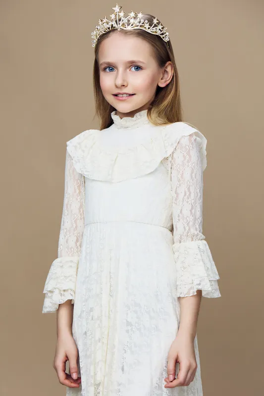 Elegant young girl in white lace dress and crown, expressing a gentle smile against a warm beige background, ideal for seasonal celebrations or fashion related themes