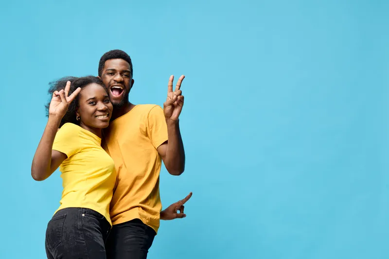 Happy young couple posing together in matching yellow shirts against a blue background, showcasing joy, friendship, and fun vibes in a festive atmosphere