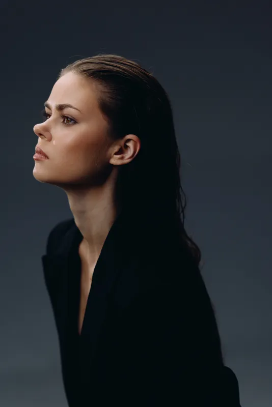 Profile of a thoughtful woman with braided hair wearing dark clothing against a muted background.