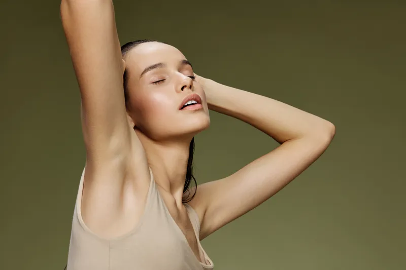 Young woman with closed eyes poses gracefully against a green background, exuding calmness and confidence in minimalistic beige clothing
