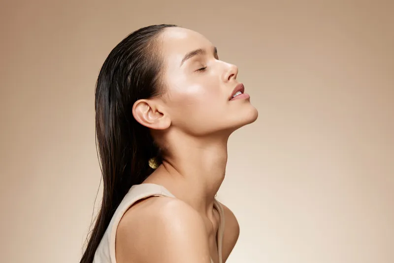 Elegant portrait of a serene young model with glossy hair, showcasing tranquility and beauty against a soft beige background, perfect for wellness and skincare concepts