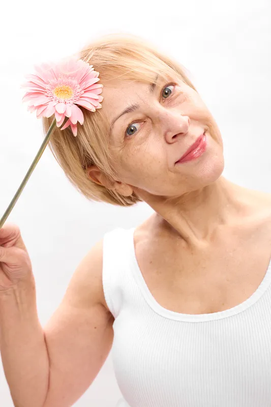 woman, flower, portrait, spring, gerbera, daisy, smiling, closeup, indoors, white background, woman face close, holding pink blossom stem, soft studio light, calm