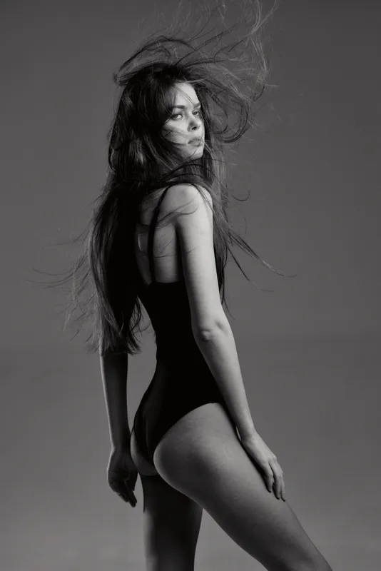 Black and white portrait of a young woman with long hair wearing a black bodysuit in dynamic pose.