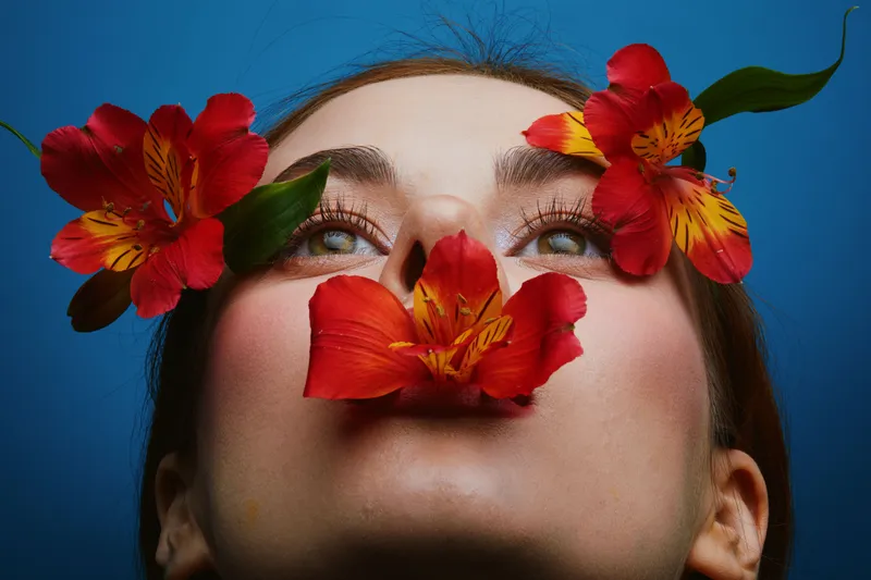 Artistic portrait of a woman with flowers, vibrant colors, expressing serenity and beauty against a blue background, highlighting seasonal floral themes
