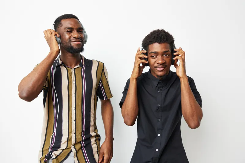 Two happy African American men enjoying music with headphones, showcasing joy and a vibrant atmosphere in their stylish outfits and lively expressions.
