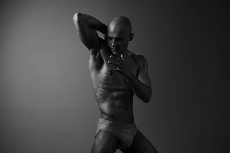 Strong man posing dramatically in a black and white setting, showcasing athleticism and emotion, highlighted by strong contrasts and shadows for visual impact.