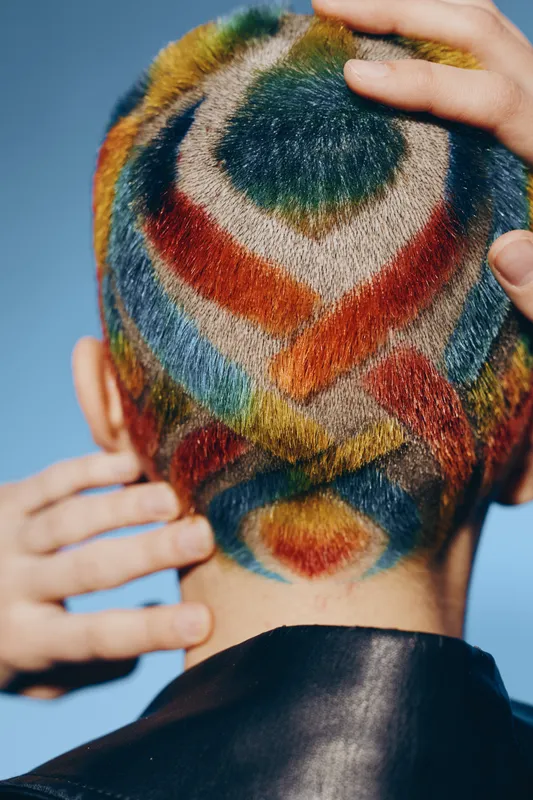 Woman with colorful geometric hair art shaved on the back of her head, displaying creative multicolor design and bold artistic expression in vivid hues.
