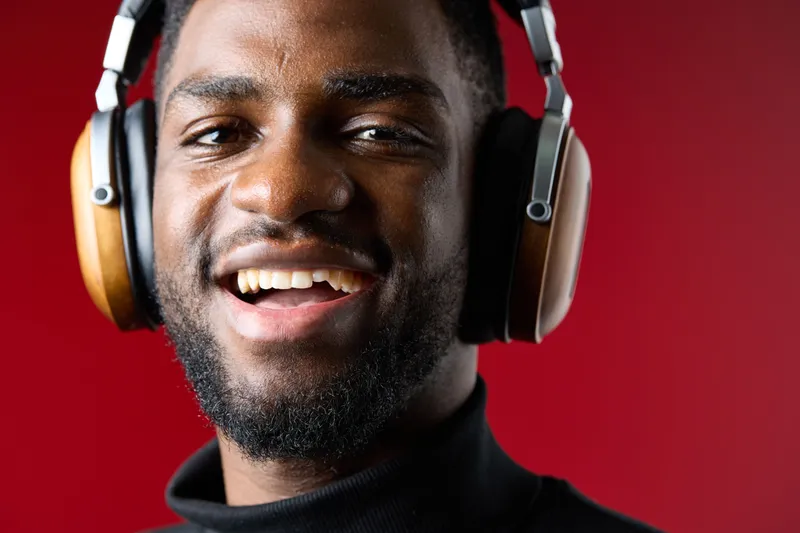 Smiling young man wearing stylish headphones against a vibrant red background, expressing joy while listening to music Perfect for concepts of enjoyment and music culture