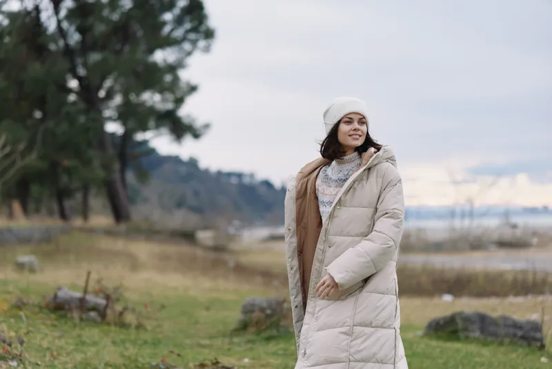 Winter woman outdoor coat landscape lake nature chilly casual fashion, serene scenic moment by the water as she wears a beanie and cozy scarf, highlighting outerwear detail and calm mood in cold