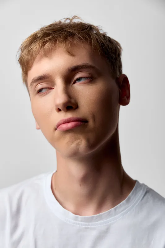 Young man, thoughtful expression, casual clothing, neutral lighting, studio shot, side profile, youthful mood, calm atmosphere, everyday wear, close up, skin texture, hair style, white tee, natural