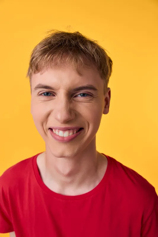 Smiling man in a red t shirt against a bold yellow background, conveying casual energy, warmth and approachability for lifestyle, marketing or fashion concepts