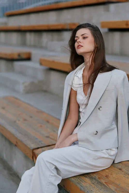 Woman in light gray business suit exhibiting confidence and elegance sitting on wooden steps outdoors with neutral background in modern fashion style