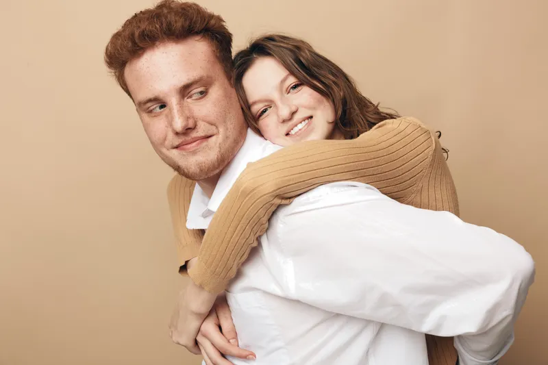 Happy young couple in casual clothes smiling and embracing each other on beige background. Concept of love, relationship, friendship, and positive emotions between people.