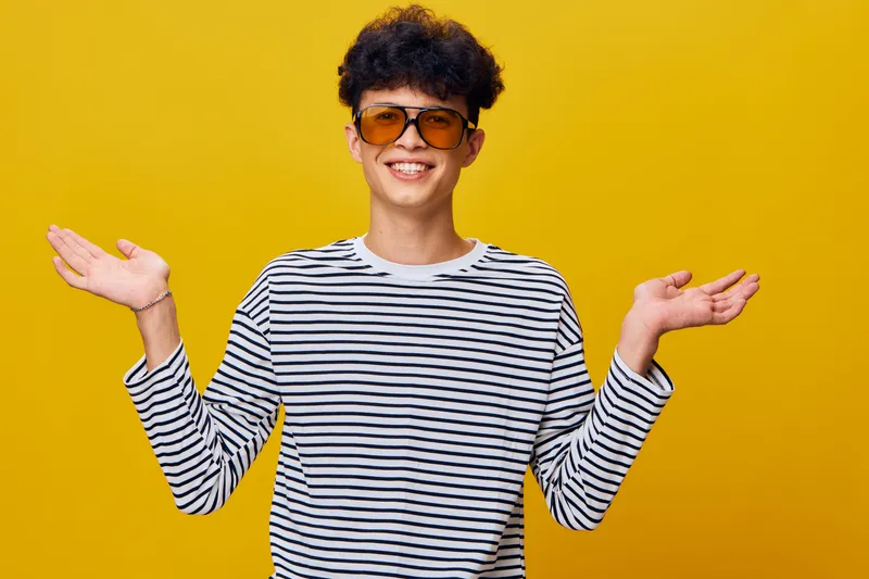 smiling man in striped shirt with sunglasses spreading hands against bright yellow background expressing confidence and friendliness in casual style