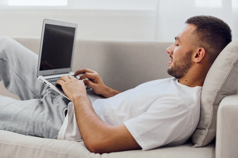 Relaxed man working on a laptop at home, wearing comfortable casual clothing. The bright, cozy environment enhances the creative atmosphere in this modern workspace.