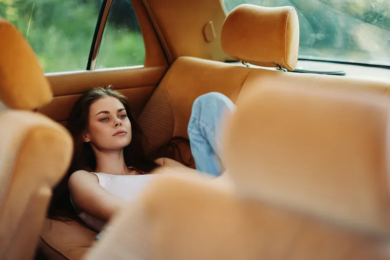 Young woman resting in a vintage car, wearing casual clothes, evoking a relaxed emotion in a natural green background, perfect for lifestyle and travel concepts.
