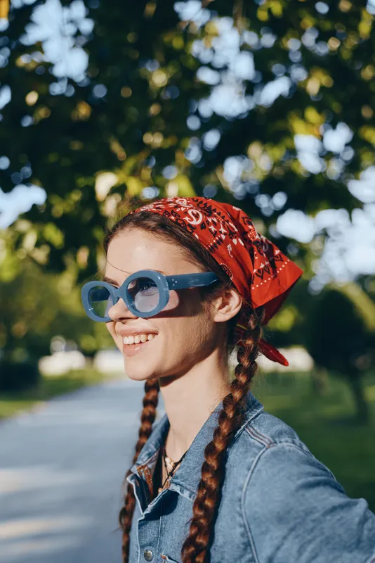 lifestyle woman with modern boho-western denim street style wearing blue sunglasses and red bandana in warm film color outdoor setting, natural smile