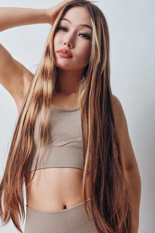Young woman with long straight hair posing with hand on head wearing sleeveless top against light background confident and stylish female portrait indoor.
