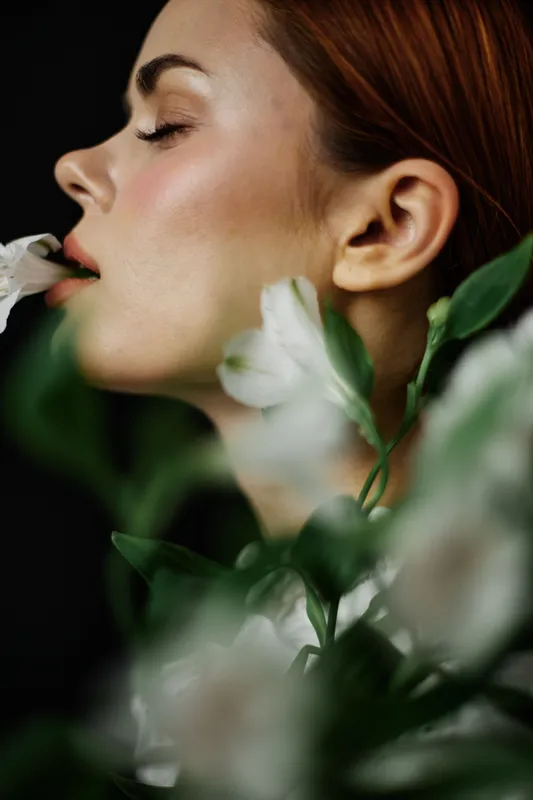 Portrait of a serene woman with closed eyes, elegantly holding a flower, surrounded by lush greenery, showcasing beauty and nature