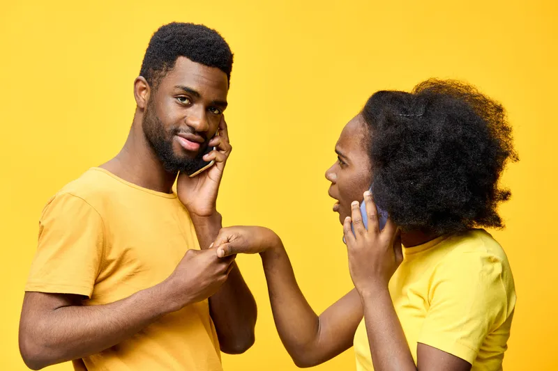 Happy couple communicating on phone against a vibrant yellow background, showcasing emotions of surprise and connection, dressed in casual yellow attire