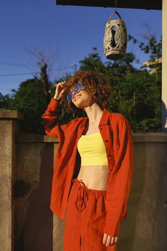Woman lifestyle portrait outdoors wearing bright yellow crop top under red jacket, posing with sunglasses, sunny atmosphere and confident mood in a summer moment